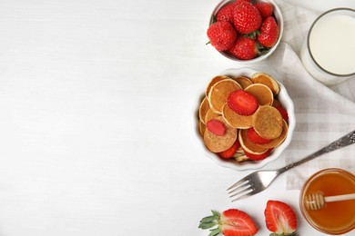 Delicious mini pancakes cereal with strawberries served on white wooden table, flat lay. Space for text
