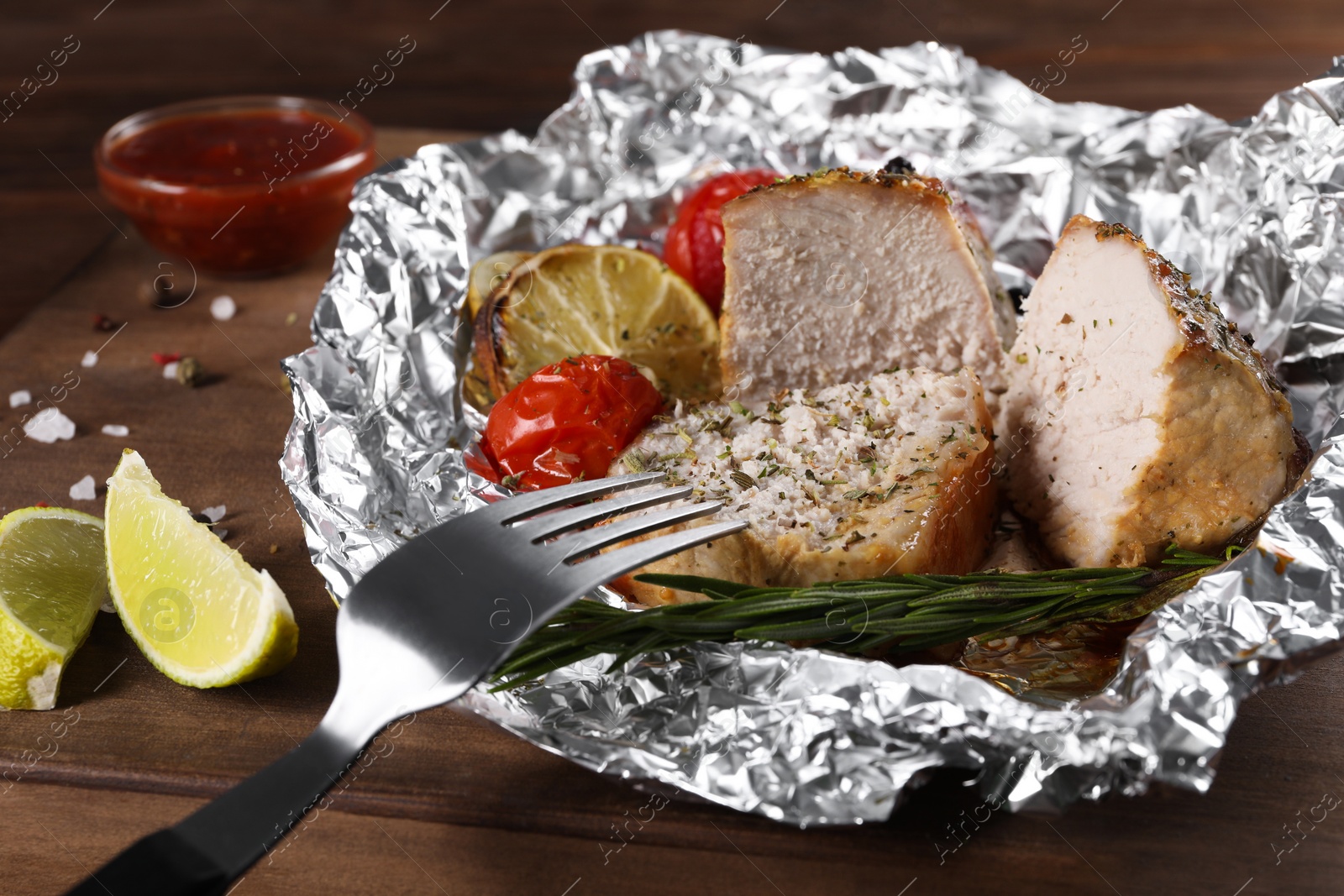 Photo of Pieces of delicious meat baked in foil with tomatoes on wooden table, closeup