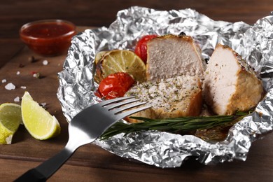 Photo of Pieces of delicious meat baked in foil with tomatoes on wooden table, closeup