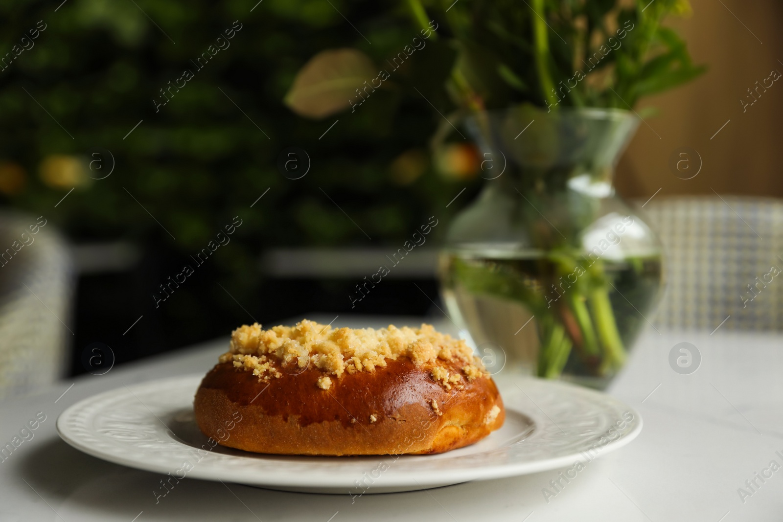 Photo of Tasty bun and vase with flowers on table in cafeteria