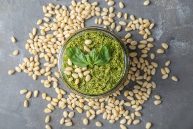 Jar with delicious pesto sauce, pine nuts and basil leaves on grey table, flat lay