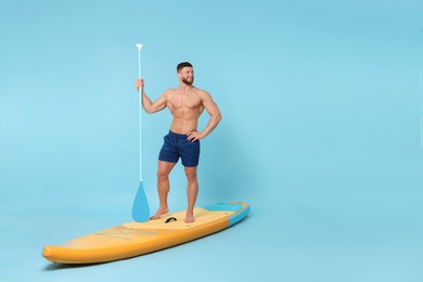 Happy man with paddle on SUP board against light blue background. Space for text