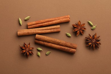 Cinnamon sticks, star anise and cardamom pods on brown background, flat lay