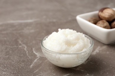 Photo of Shea butter in bowl and nuts on grey background. Space for text