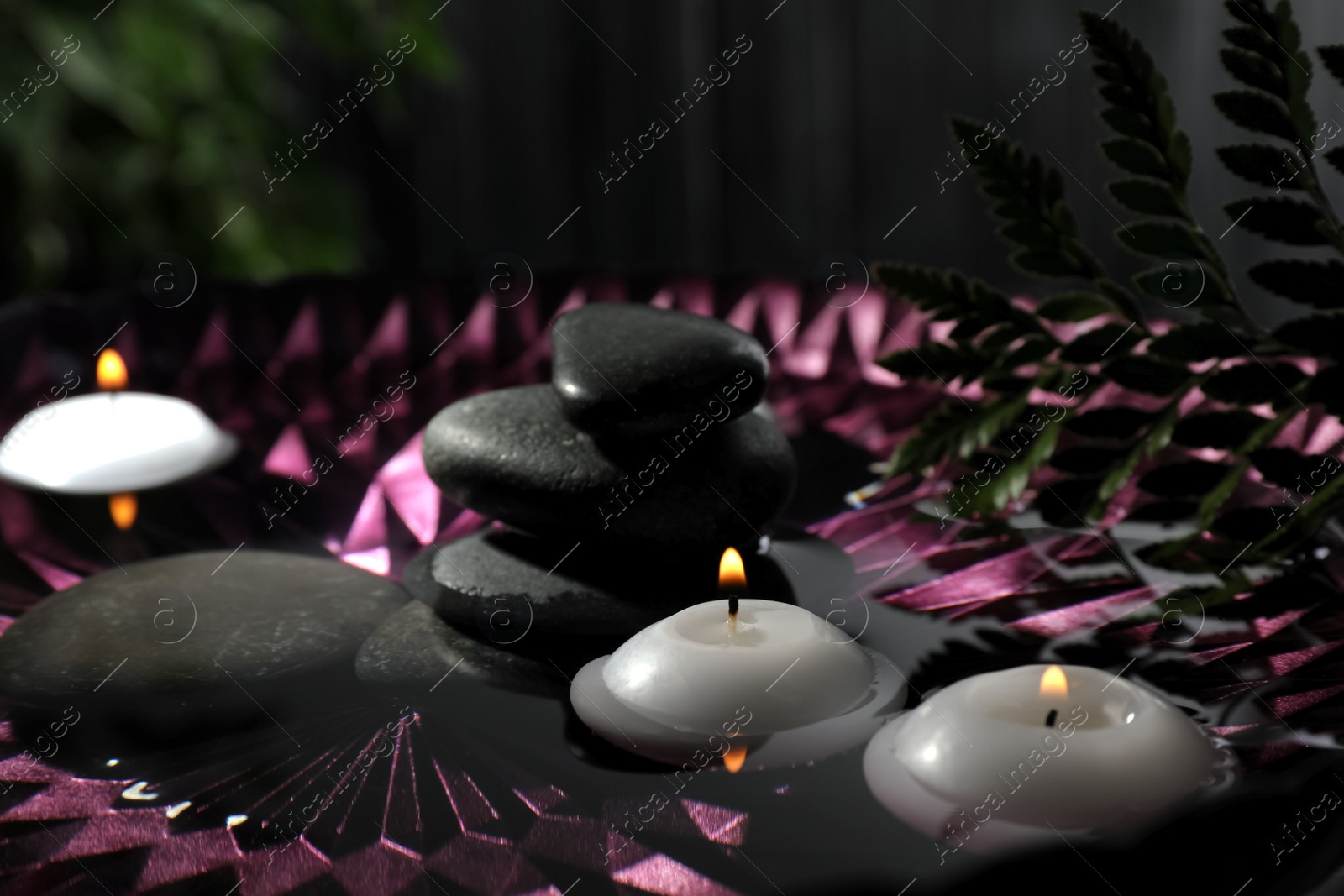 Photo of Burning candles and spa stones in bowl with water, closeup
