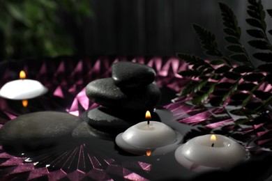 Burning candles and spa stones in bowl with water, closeup