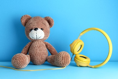Baby songs. Toy bear and yellow headphones on light blue background