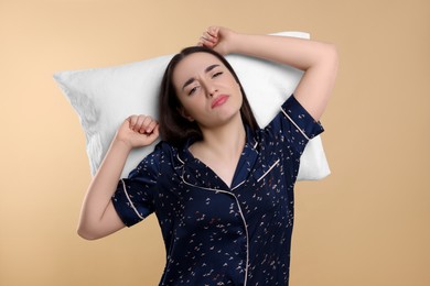 Photo of Tired young woman with pillow on beige background. Insomnia problem