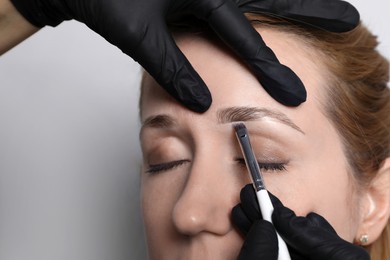 Photo of Beautician applying tint during eyebrows correction procedure on light grey background, closeup