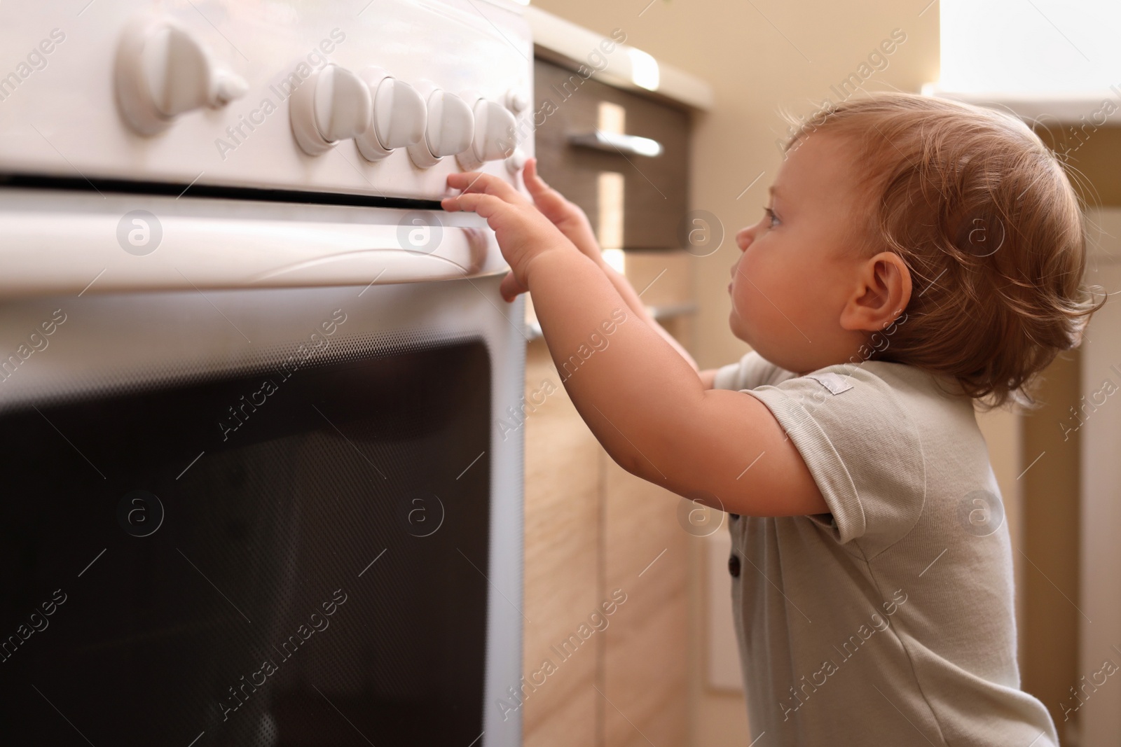 Photo of Little child playing with gas stove indoors. Dangers in kitchen