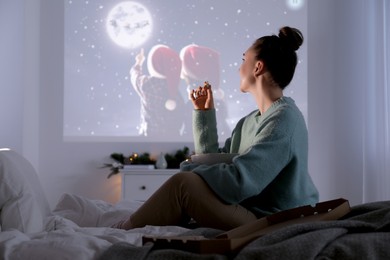 Photo of Woman with popcorn watching Christmas movie via video projector at home