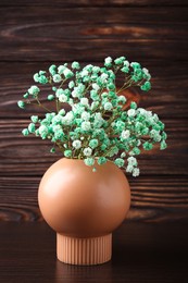 Beautiful dyed gypsophila flowers in stylish vase on wooden table