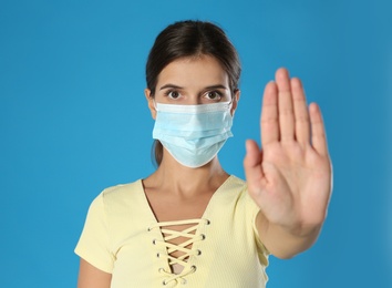 Photo of Woman in protective mask showing stop gesture on blue background, space for text. Prevent spreading of coronavirus