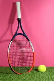 Tennis racket and ball on on green grass against pink background. Sports equipment