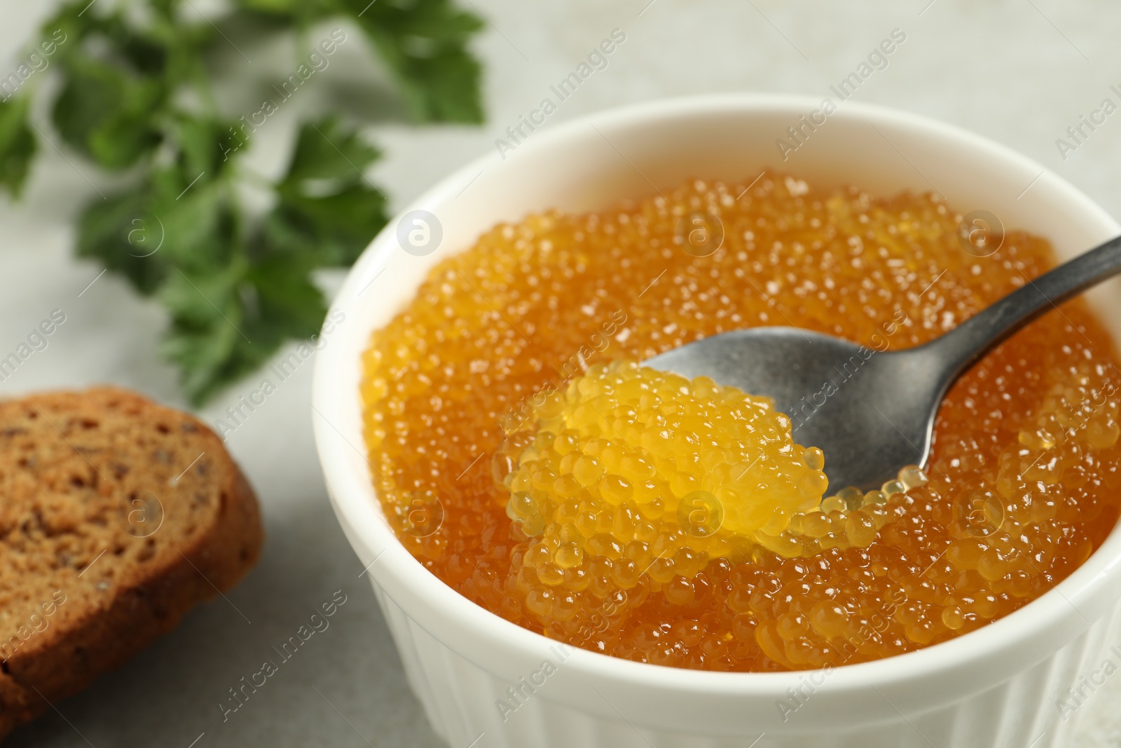 Photo of Fresh pike caviar in bowl, parsley and bread on light grey table, closeup