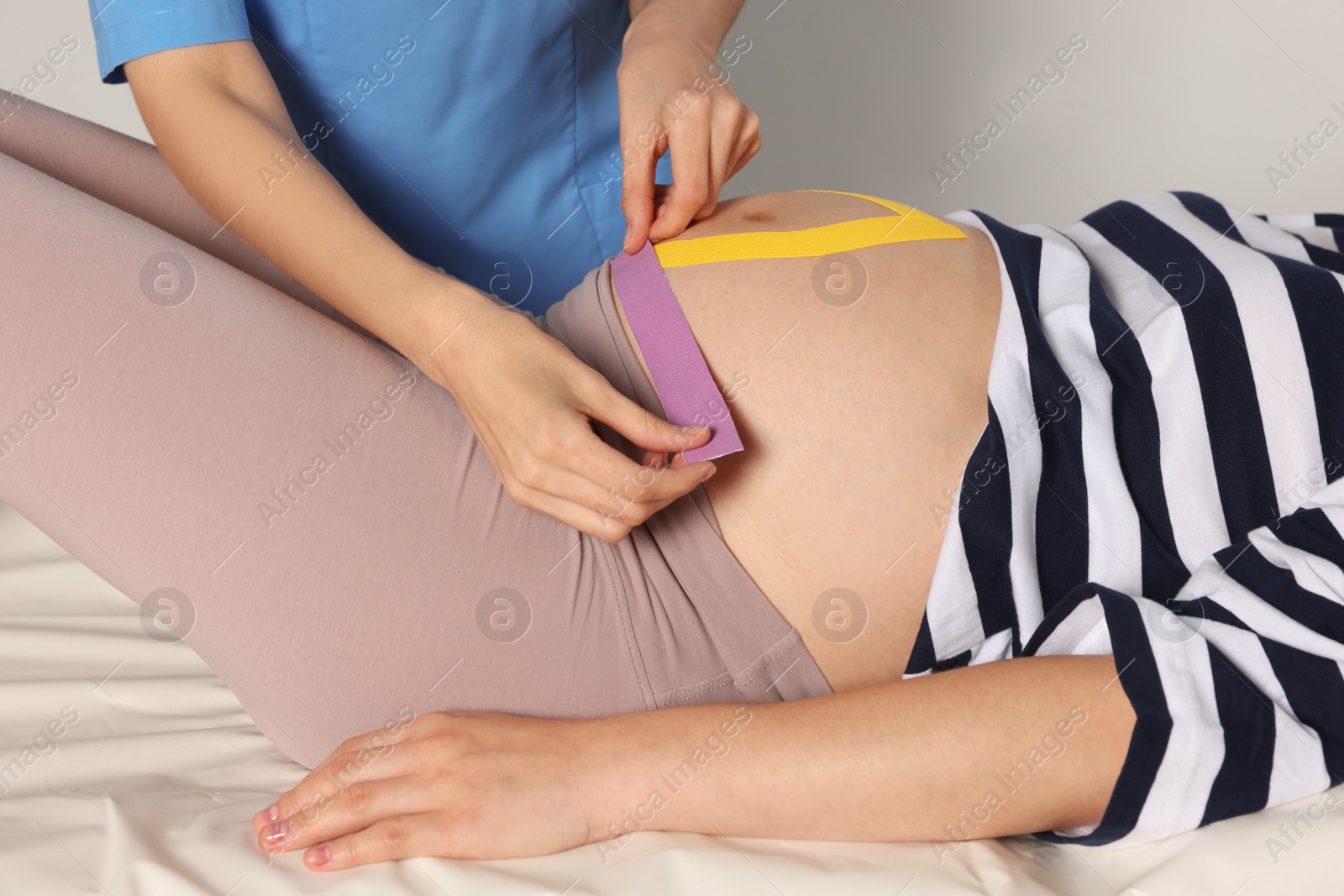 Photo of Pregnant woman visiting physiotherapist. Doctor applying kinesio tape on couch, closeup