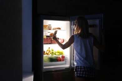 Photo of Woman taking sandwich out of refrigerator in kitchen at night