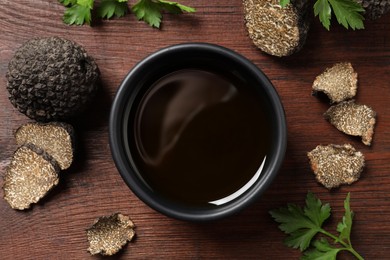Photo of Fresh truffles, oil in bowl and parsley on wooden table, flat lay