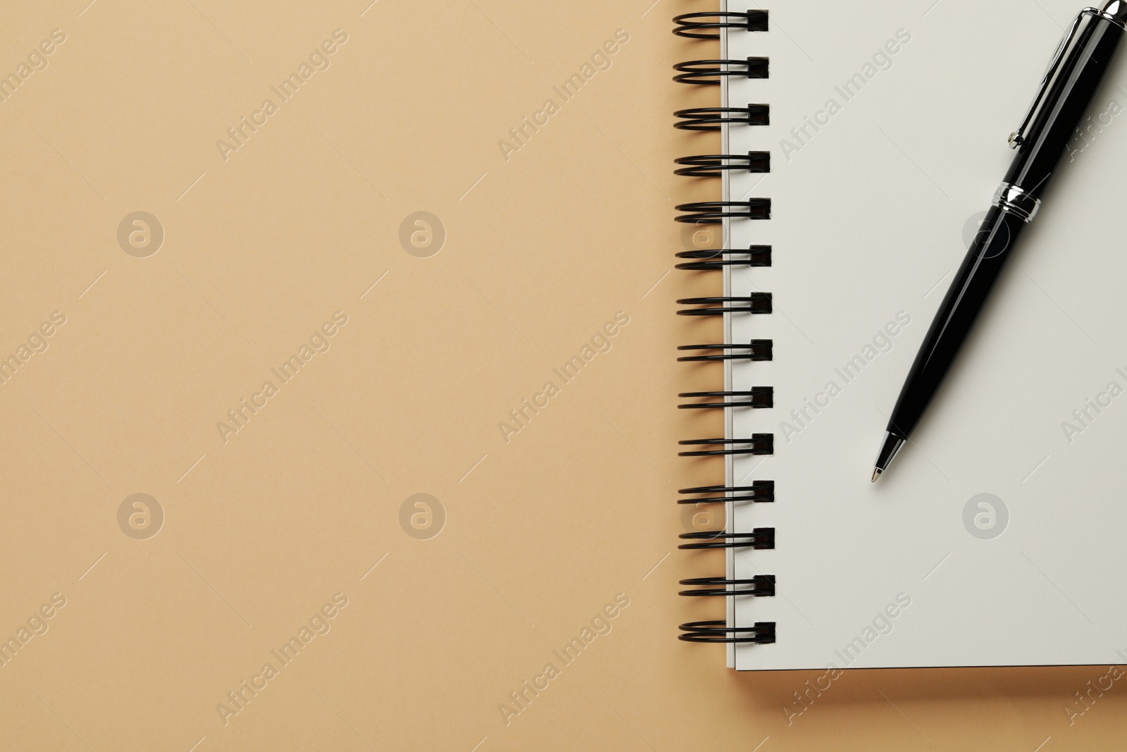 Photo of Notebook and pen on beige background, top view. Space for text