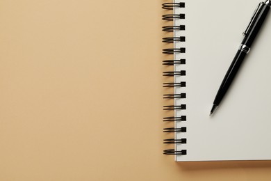 Photo of Notebook and pen on beige background, top view. Space for text