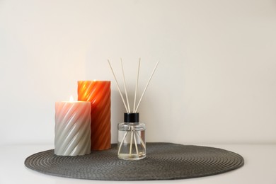 Photo of Aromatic reed air freshener and burning candles on white table