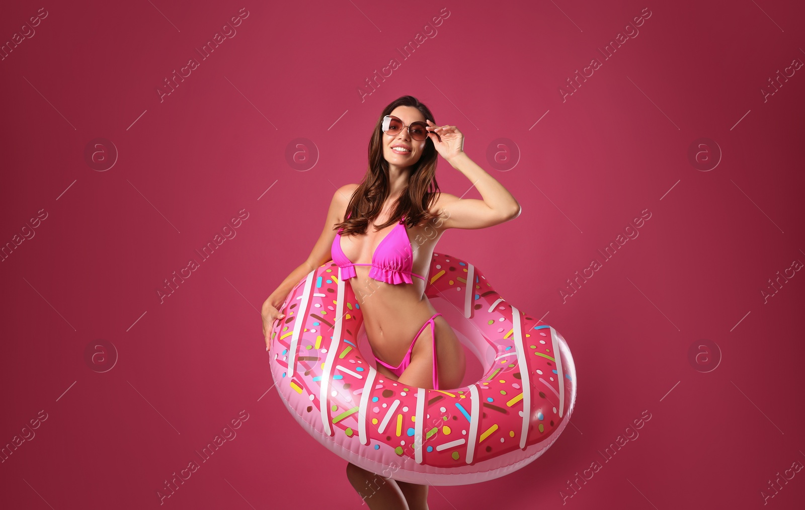 Photo of Beautiful woman in stylish bikini with inflatable ring on crimson background