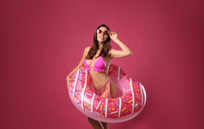 Photo of Beautiful woman in stylish bikini with inflatable ring on crimson background