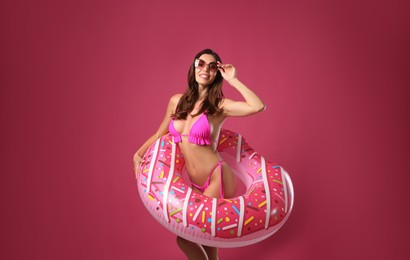 Beautiful woman in stylish bikini with inflatable ring on crimson background