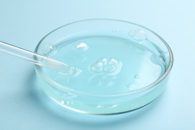 Photo of Petri dish with liquid sample and pipette on light blue background, closeup