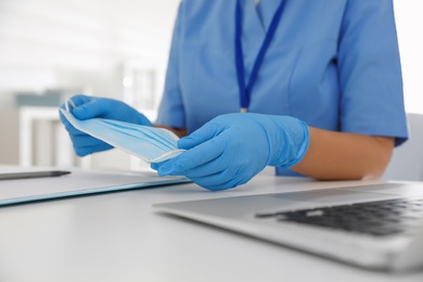 Photo of Doctor in medical gloves holding protective mask at table in office, closeup