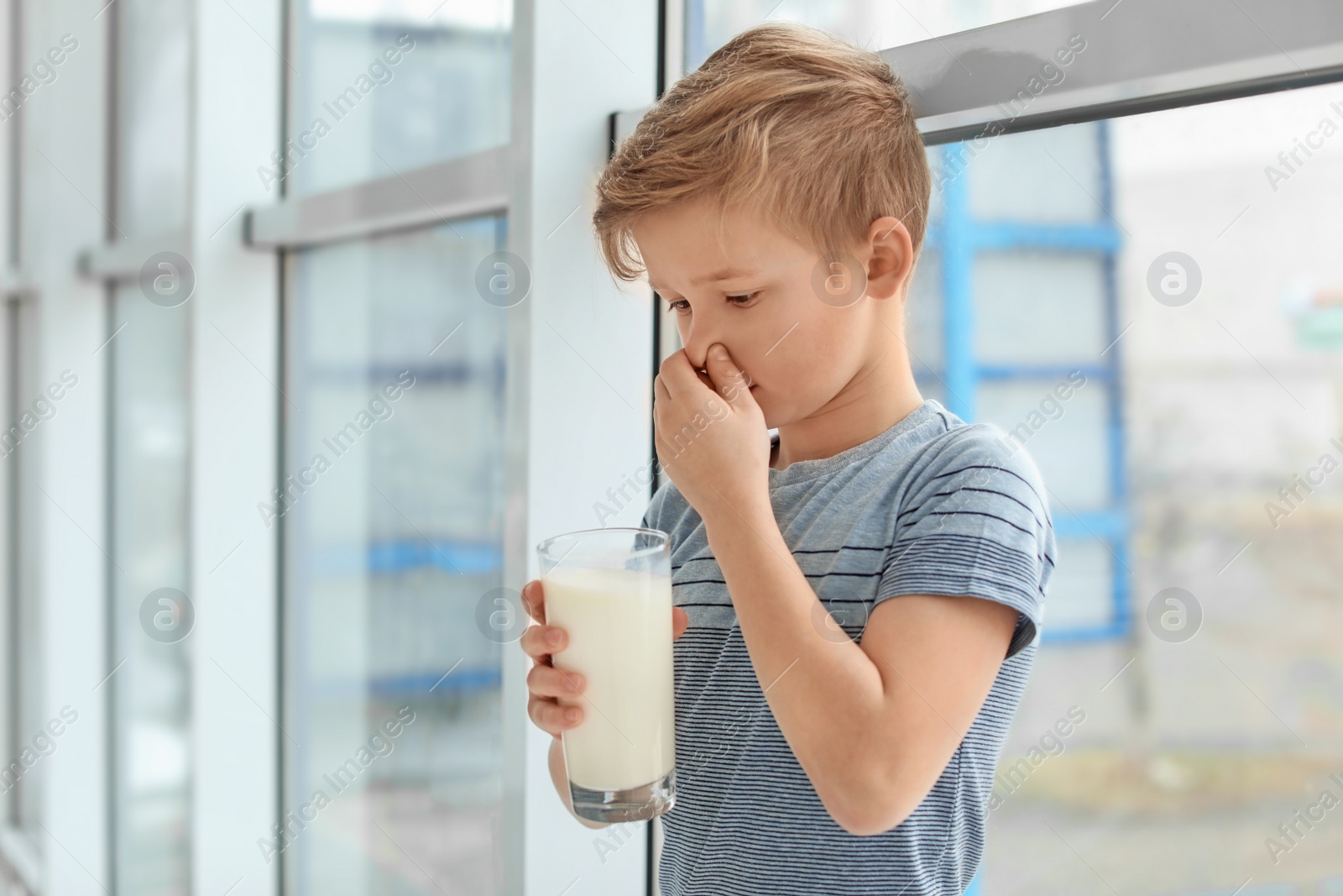 Photo of Little boy with dairy allergy holding glass of milk indoors
