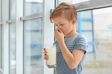 Little boy with dairy allergy holding glass of milk indoors