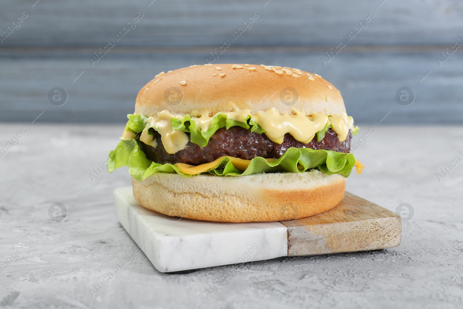 Photo of Delicious cheeseburger on grey textured table, closeup