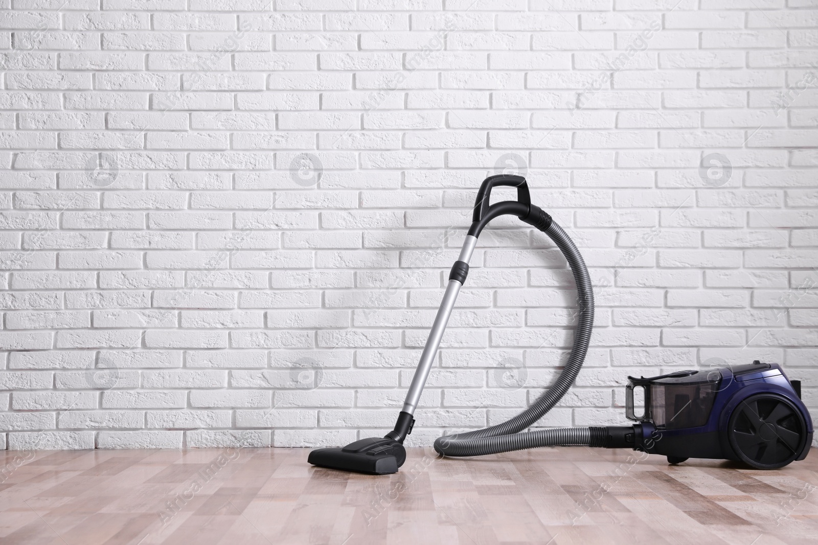 Photo of Modern vacuum cleaner near white brick wall indoors, space for text