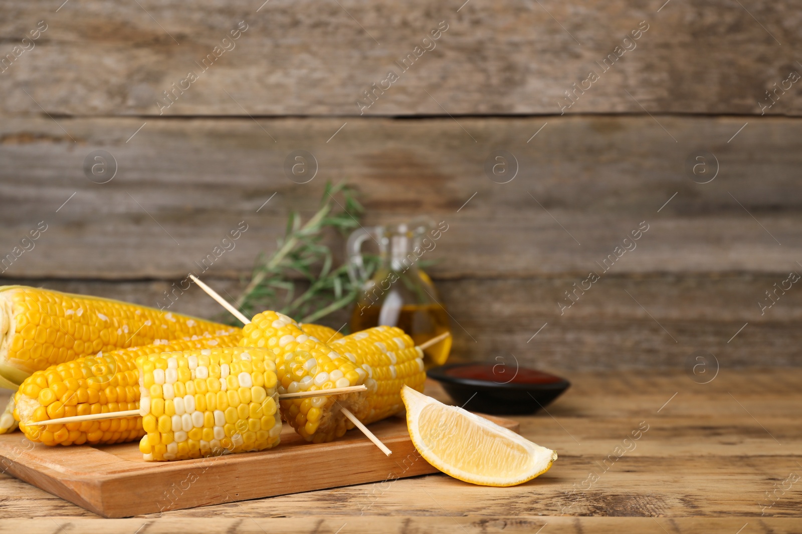 Photo of Tasty corn cobs and lemon on wooden table, space for text