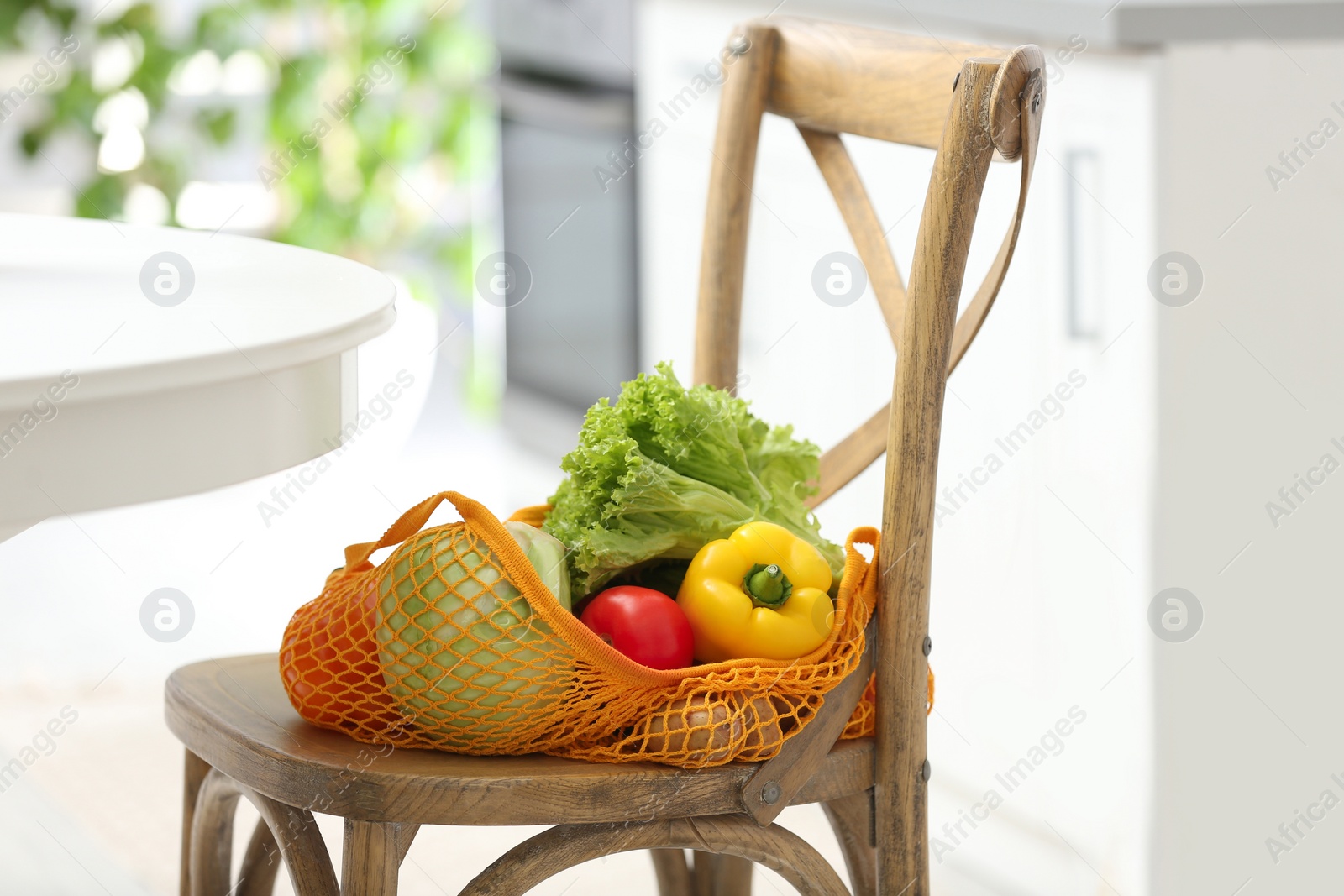 Photo of Net bag with vegetables on wooden chair in kitchen