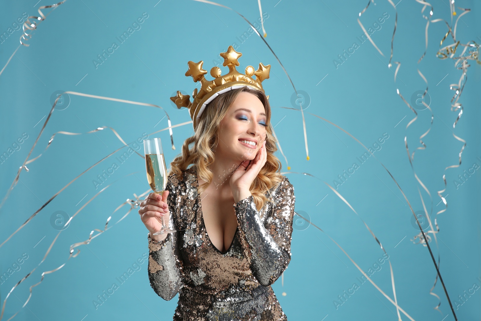 Photo of Happy woman with champagne and falling down serpentines on light blue background