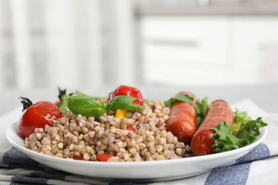 Plate with tasty buckwheat porridge and sausages indoors, closeup