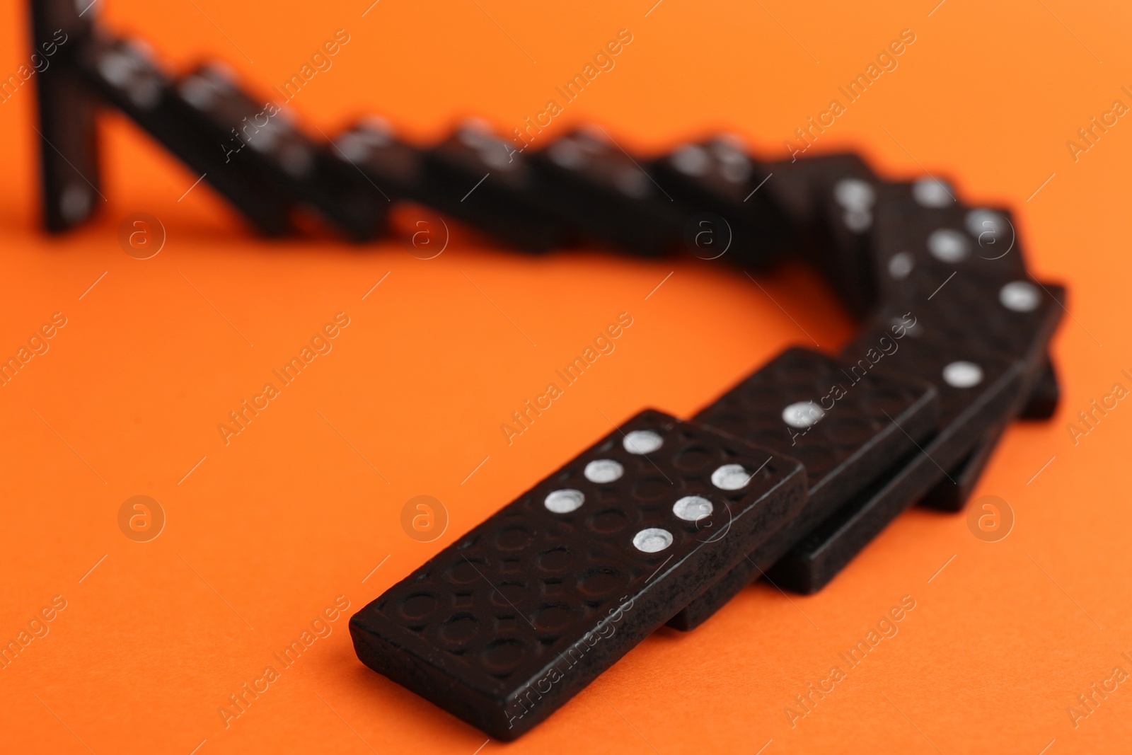 Photo of Brown domino tiles falling on orange background, closeup