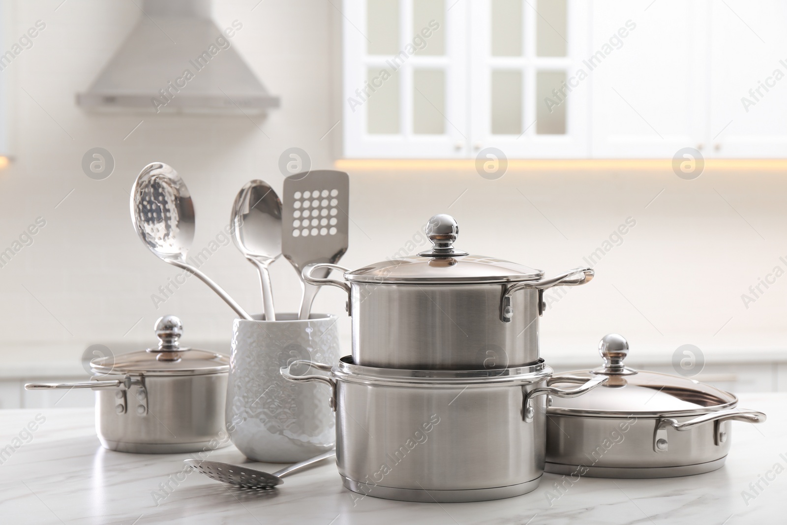 Photo of Set of stainless steel cookware and kitchen utensils on white table indoors