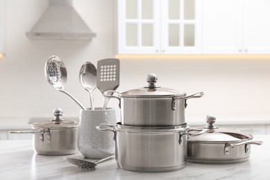 Photo of Set of stainless steel cookware and kitchen utensils on white table indoors