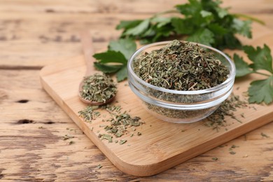 Photo of Bowl and spoon with dried parsley on wooden table, closeup. Space for text