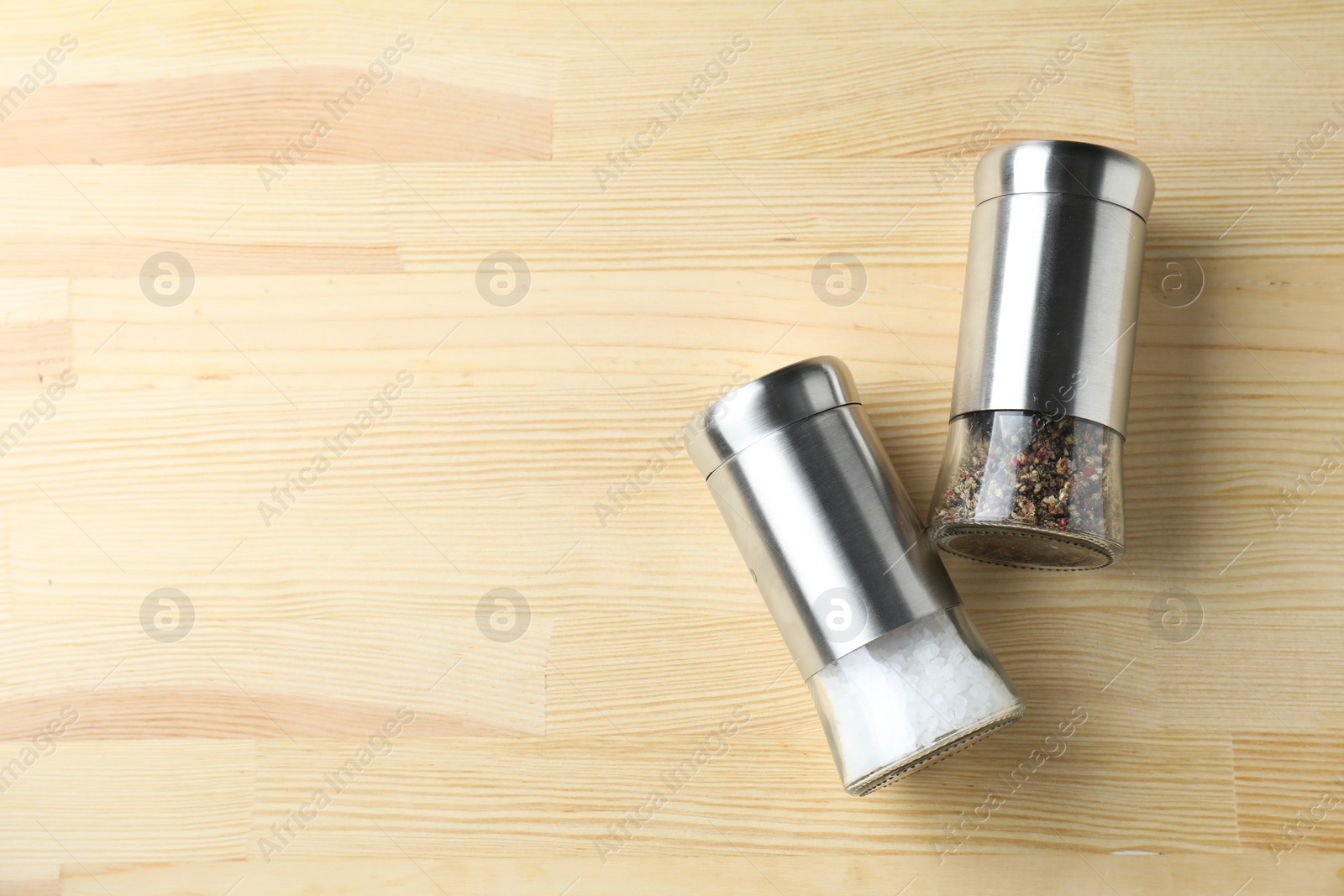 Photo of Salt and pepper shakers on light wooden table, top view. Space for text