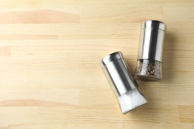 Photo of Salt and pepper shakers on light wooden table, top view. Space for text
