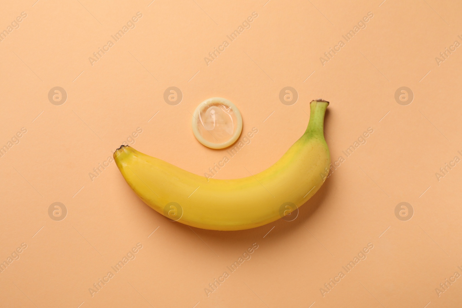 Photo of Banana with condom on pale orange background, flat lay. Safe sex concept