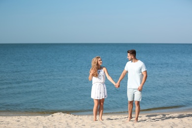 Happy young couple holding hands at beach on sunny day