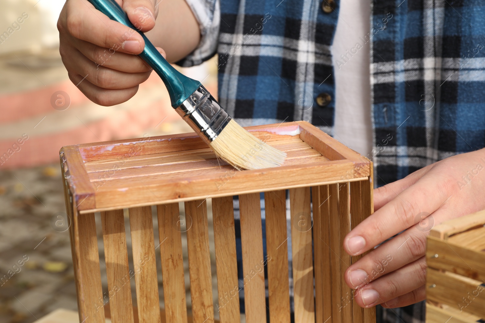 Photo of Man applying varnish onto wooden crate against blurred background, closeup