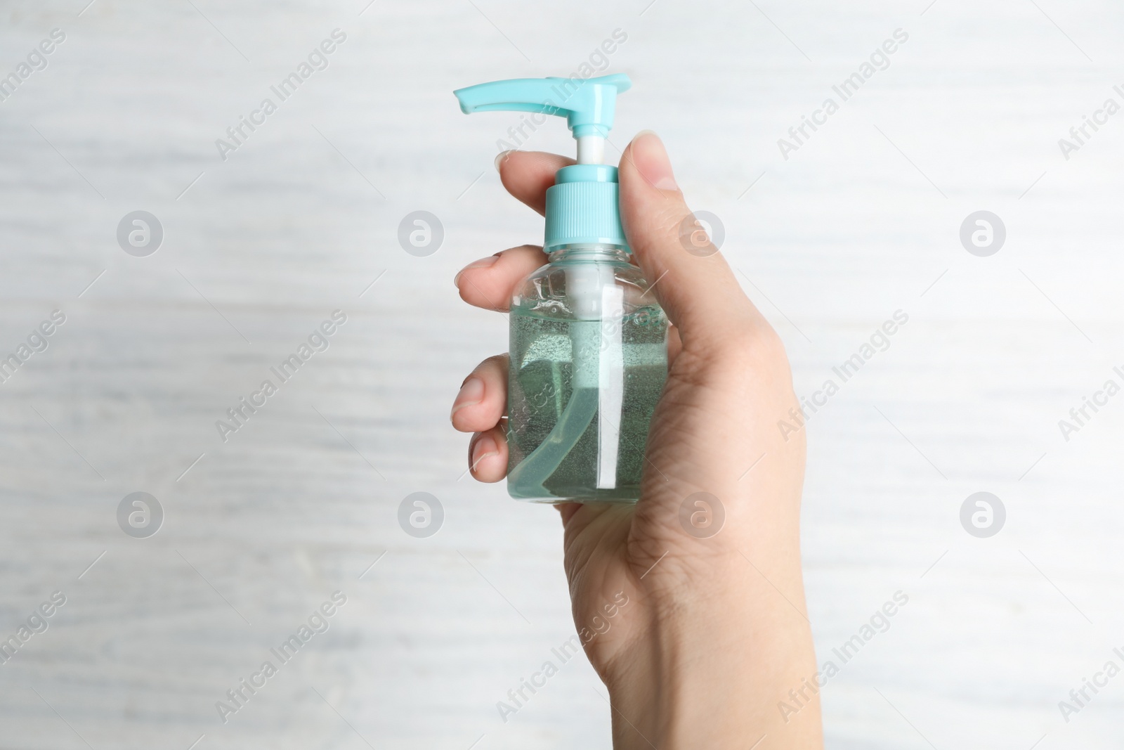 Photo of Woman holding antiseptic gel on light background, closeup