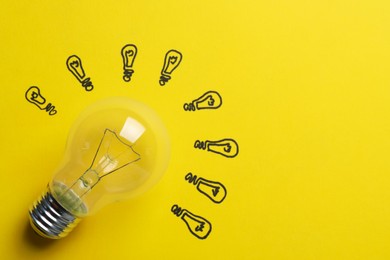 Photo of Many drawn lightbulbs and real one on yellow background, top view. Space for text