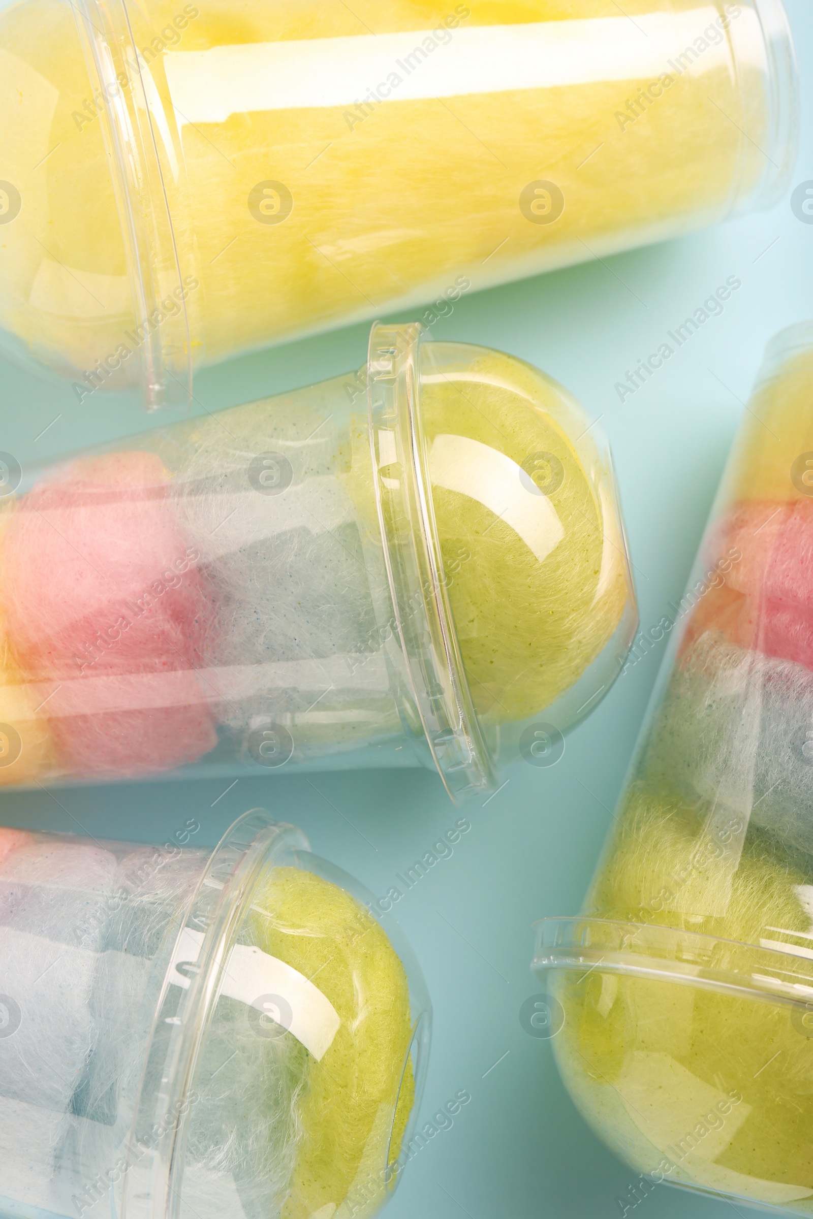 Photo of Colorful cotton candies in plastic cups on light blue background, flat lay